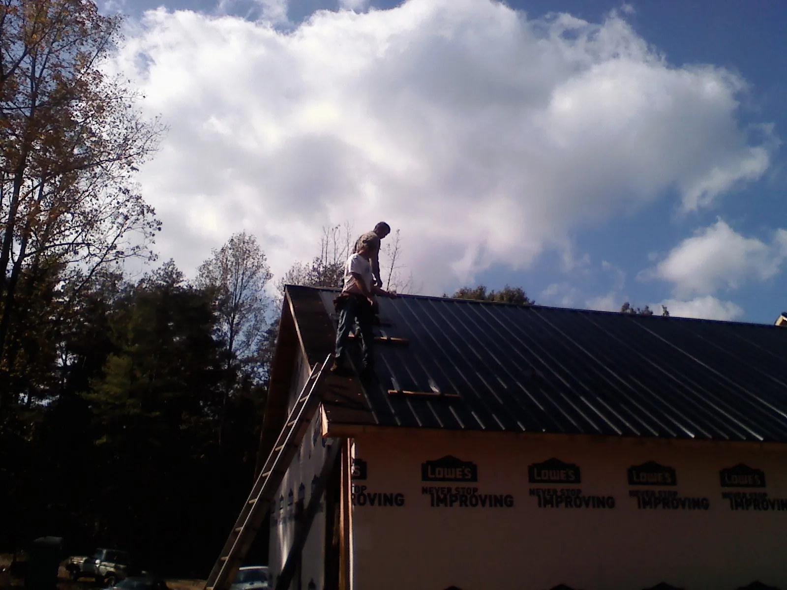 Roofer fastening dark metal panels high against a cloudy sky, from a Roof Inspection job in Frackville