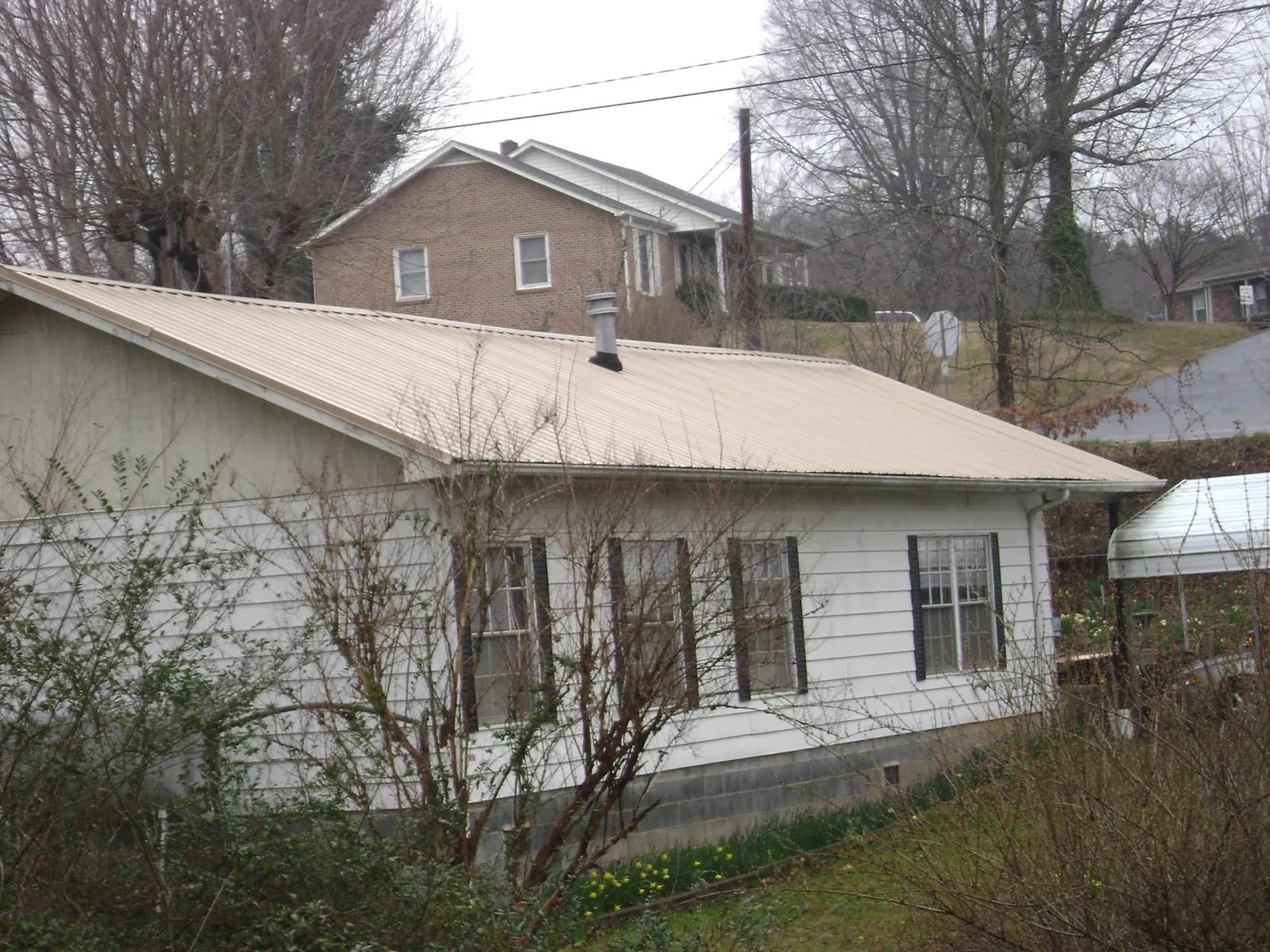 Tan metal roof on a white sided house set into a hillside — Commercial Roofing by Roofing Brothers in Frackville